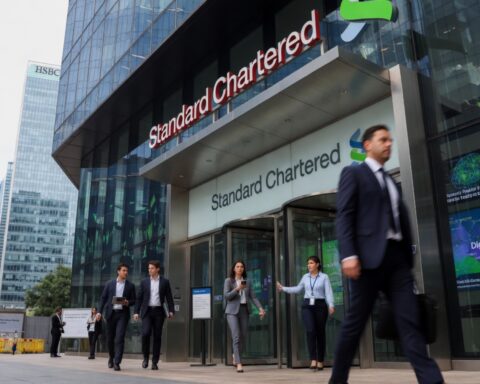 Employees walk past the Standard Chartered headquarters building in a modern financial district as the bank announces major AI-driven job cuts and restructuring plans.